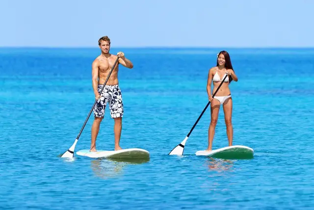 Two people standing on paddle boards on calm blue water